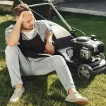 Man cutting grass with lawn mover in the back yard. male in a black apron.